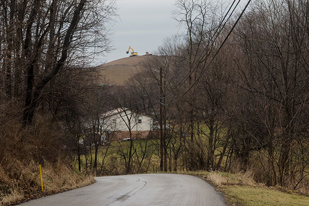 An excavator is seen at the top of the slope to the MAX landfill site. A home is in view in the foreground.