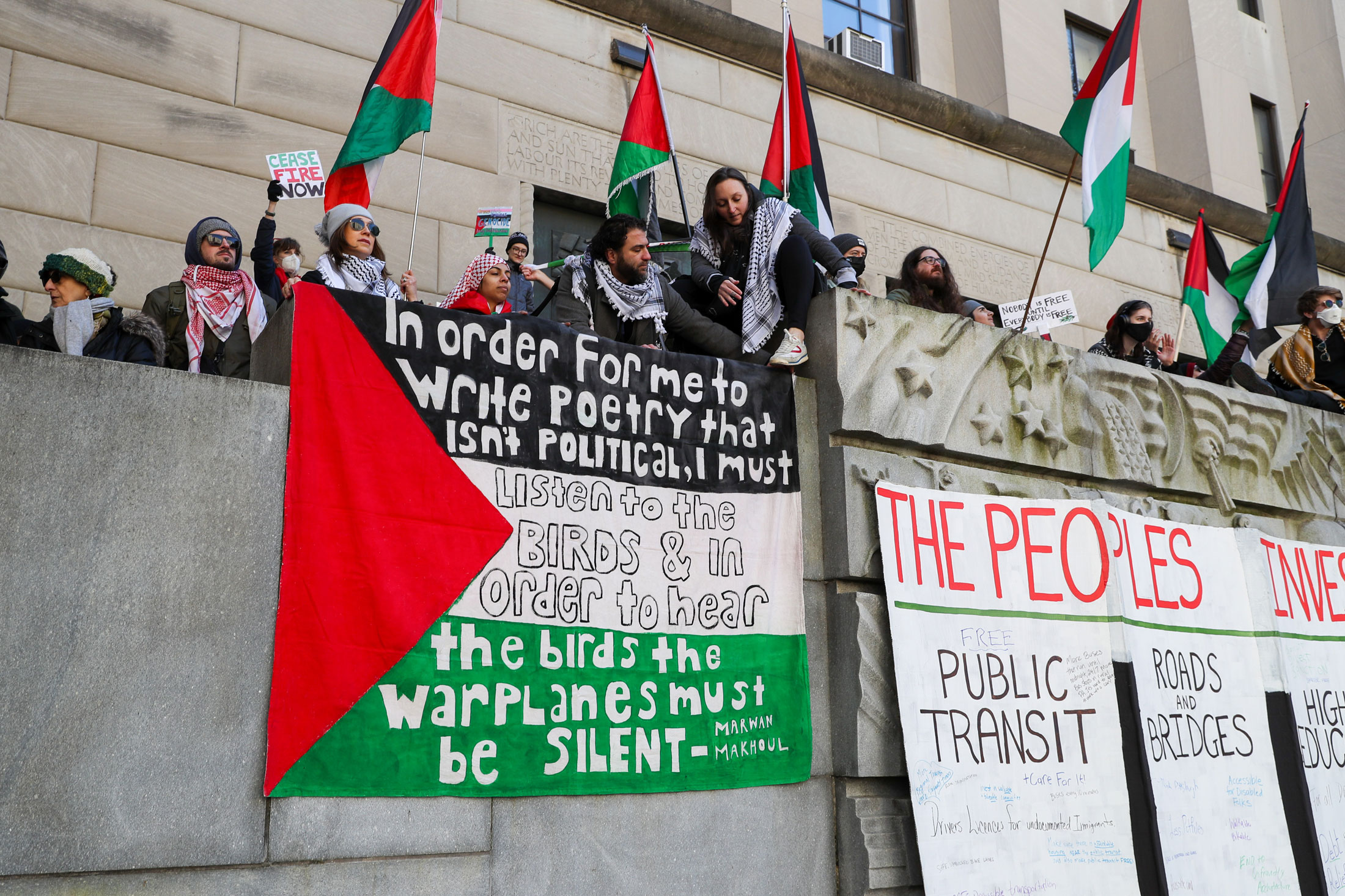 Protesters hold banners and flags outside Garrity’s office as they call for the state to divest state money from Israel bonds.